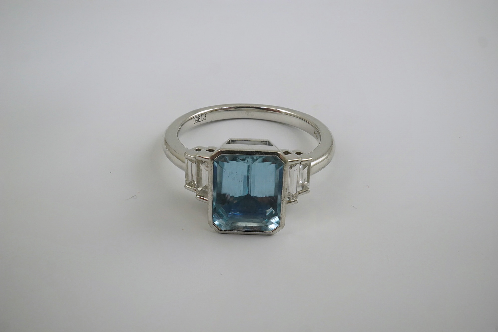 An Art Deco style platinum and single stone emerald cut aquamarine set dress ring, with four stone graduated baguette cut diamond set shoulders